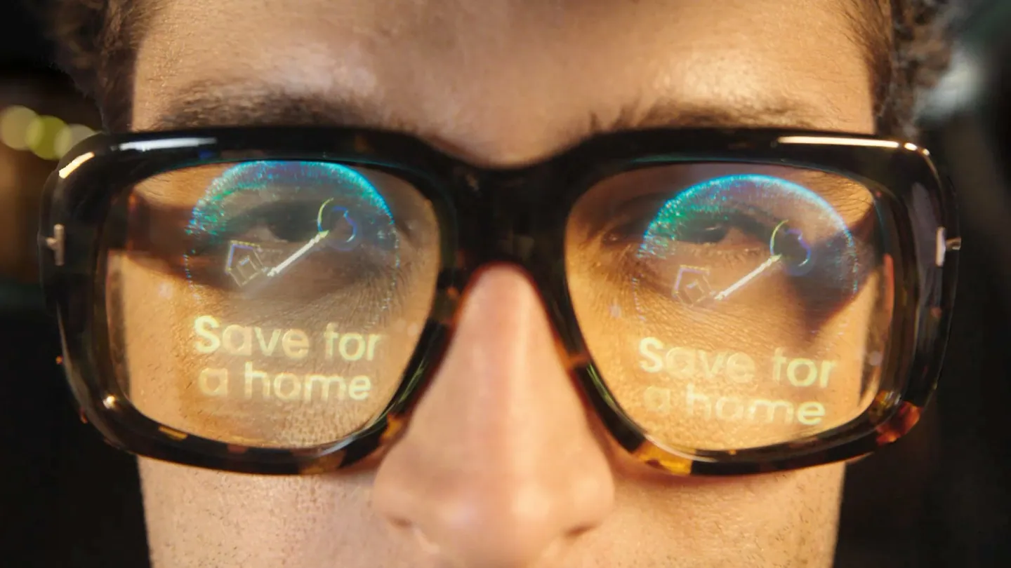 Close-up of a driver's glasses reflecting a floating “Save for a home” milestone.