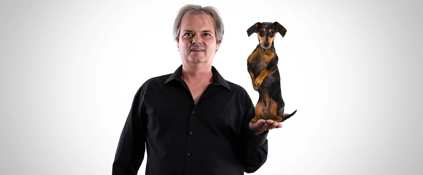 Team portrait: a man in black holding a small dog on his shoulder.